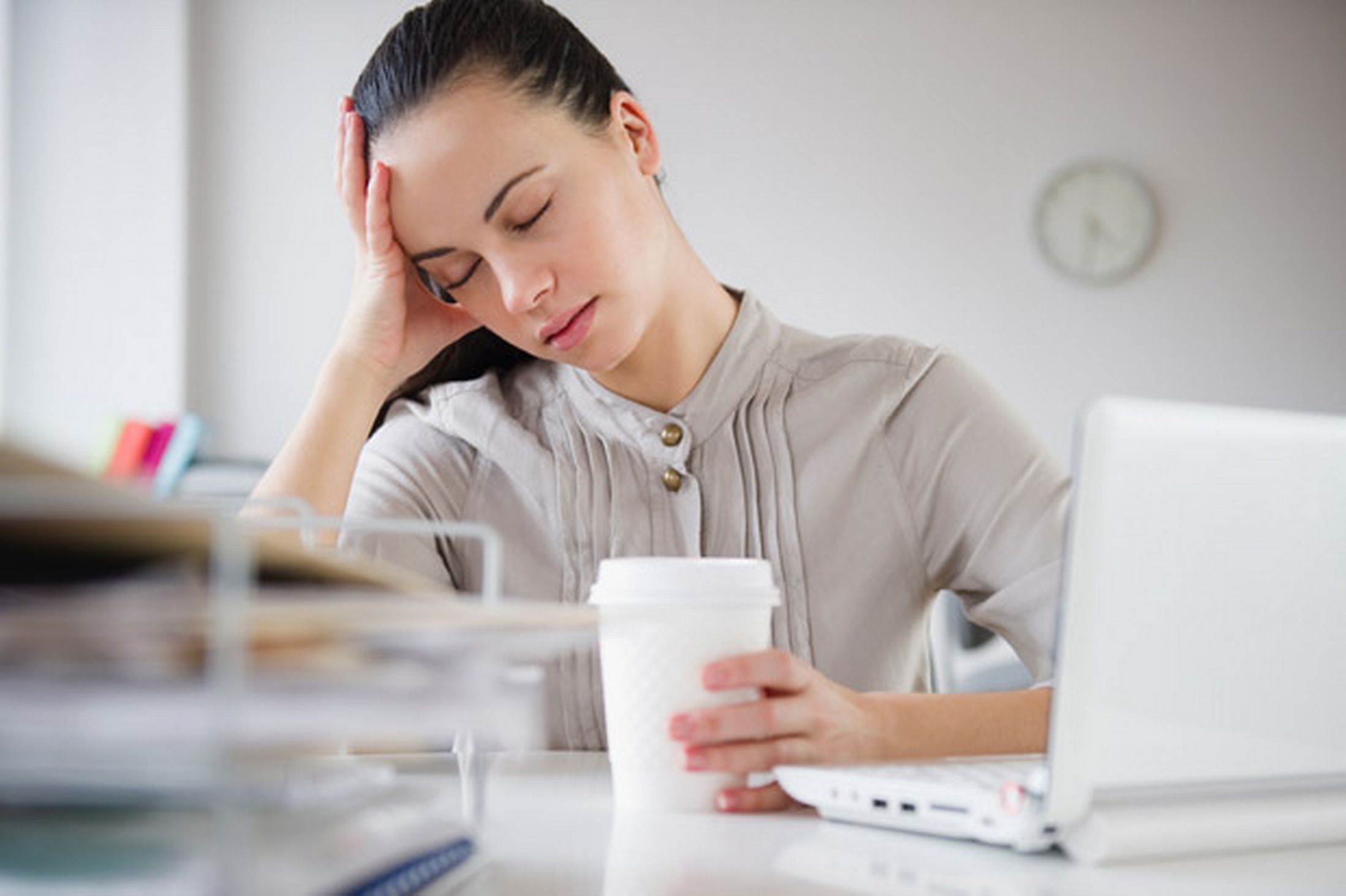 a-woman-exhausted-sitting-at-her-desk-with-a-cup-of-coffee