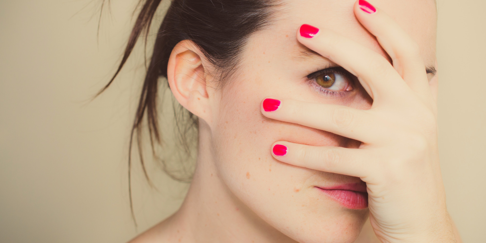 Misterious girl with red nails and hand on face.