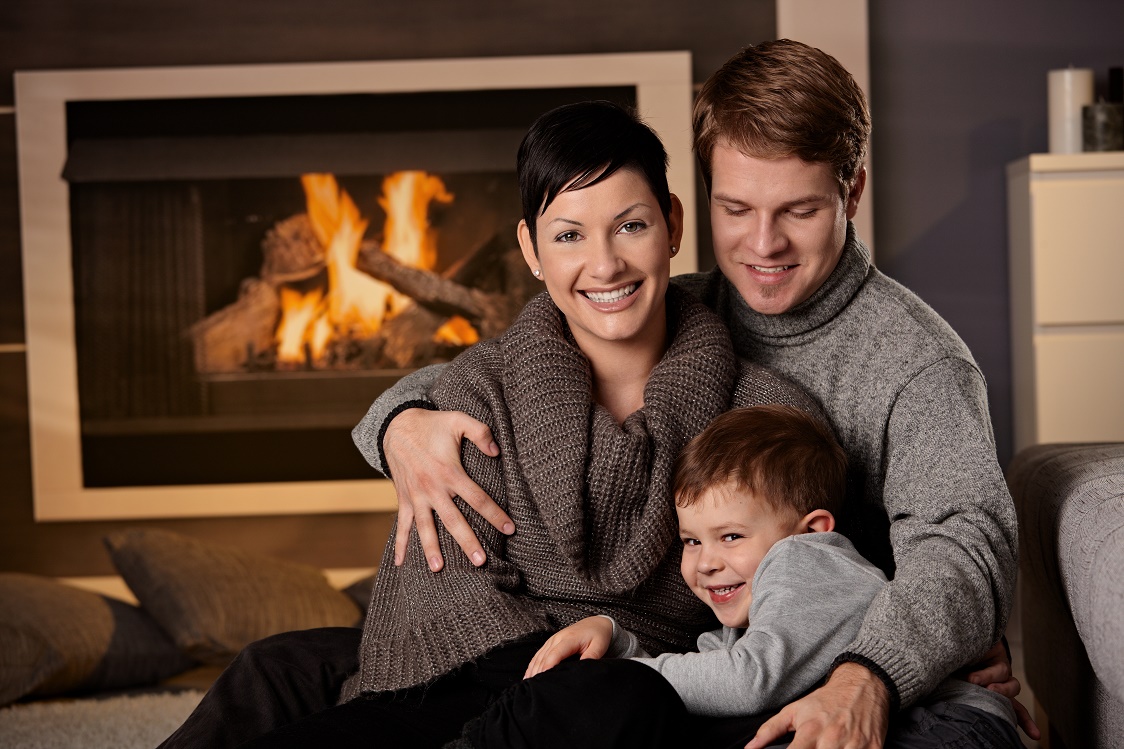 Happy family sitting on couch at home in a cold winter day looking at camera smiling.