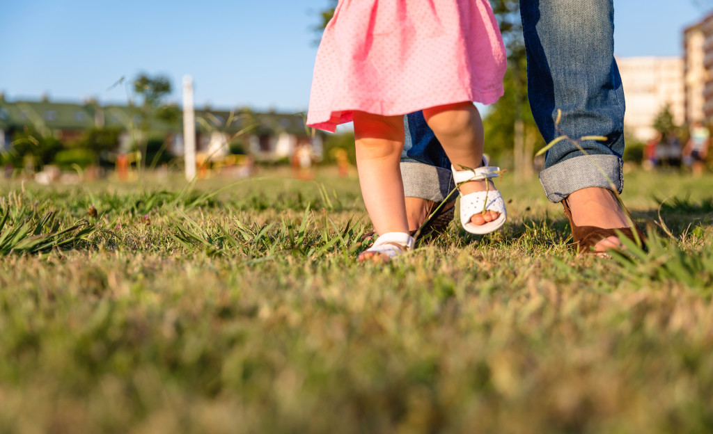 Adorable baby girl learning to walk with his mother on the grass park in a sunny summer day